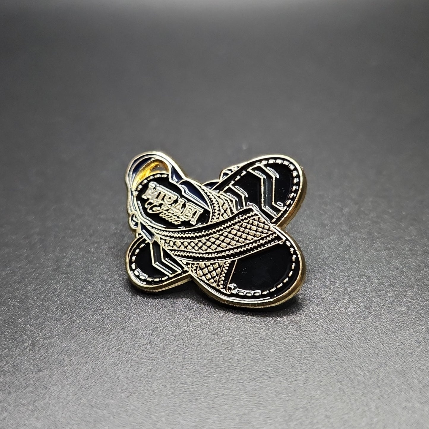 Two pieces of shoe accessories, one in gold and one in silver, with a geometric pattern and the brand 'MIYAGI' inscribed on the gold piece.